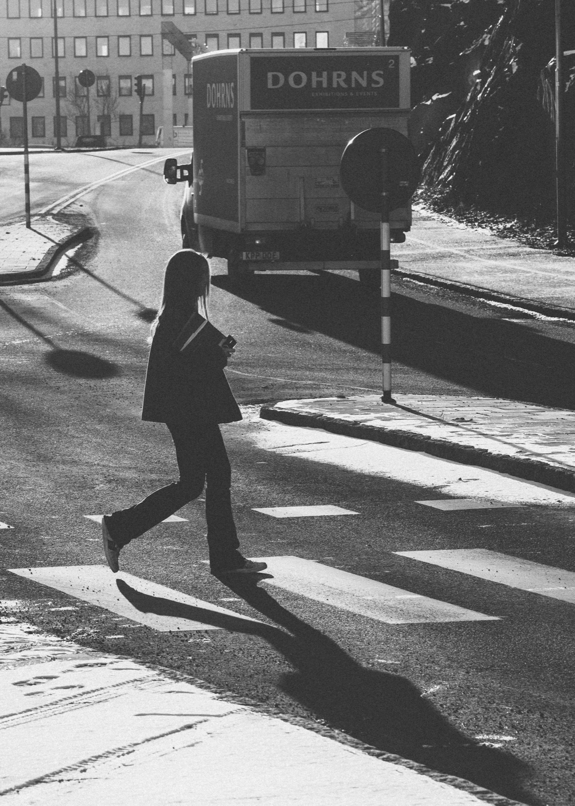 Black and white street photograph with a pedestrian and long afternoon shadow