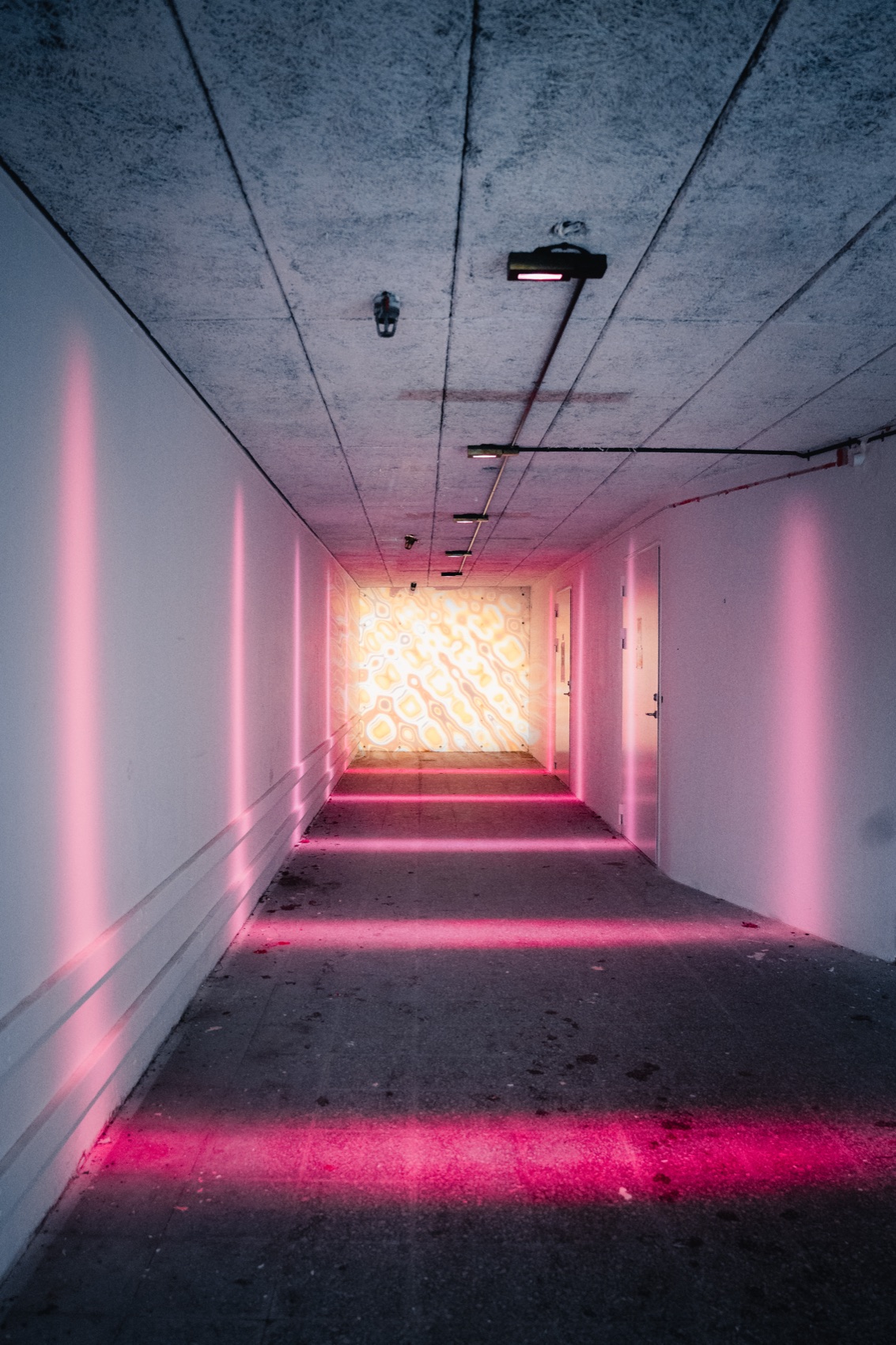 A pink-lit corridor extending toward an illuminated wall