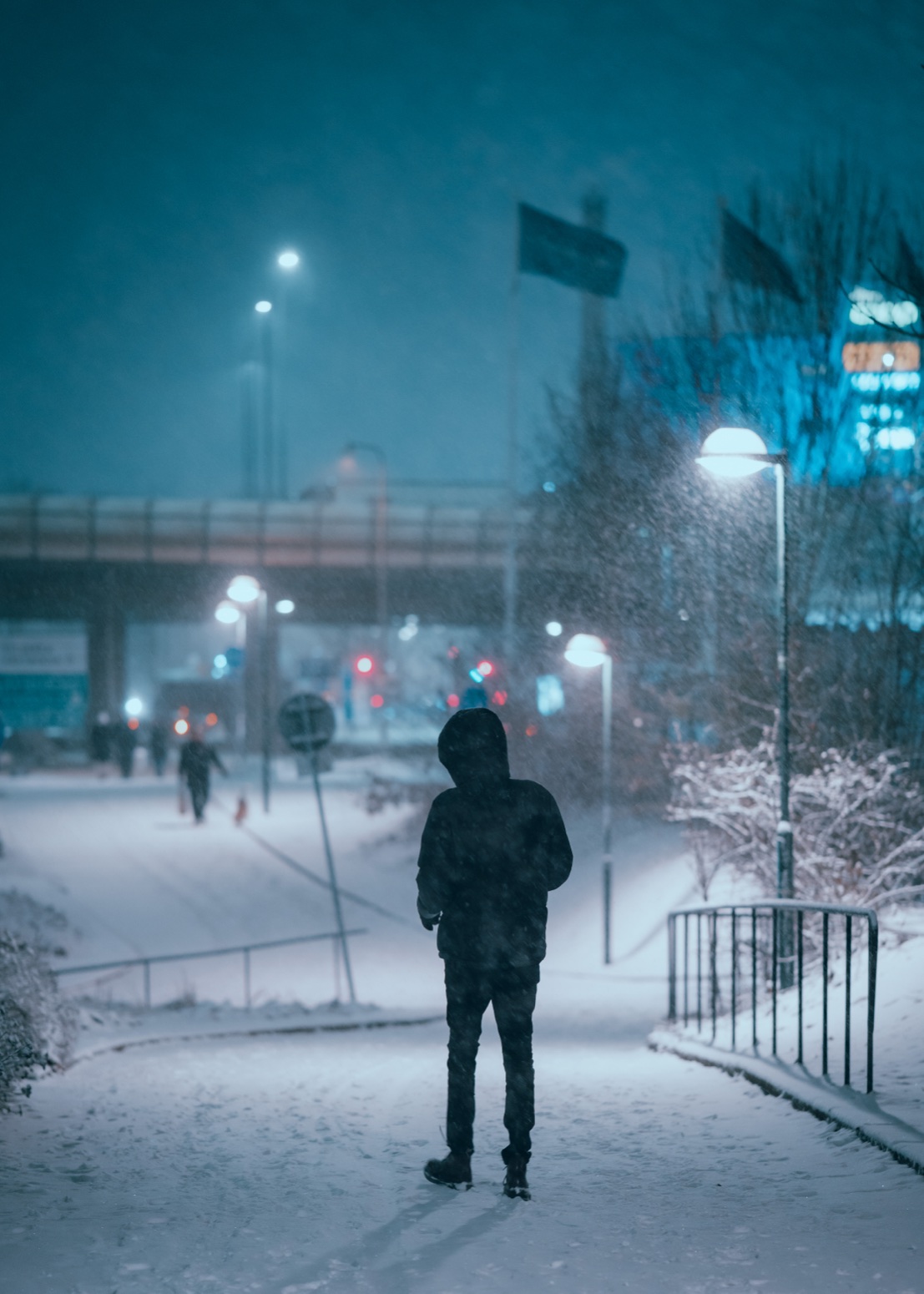 A lone silhouette in a snow-covered street at night under blue street lamps